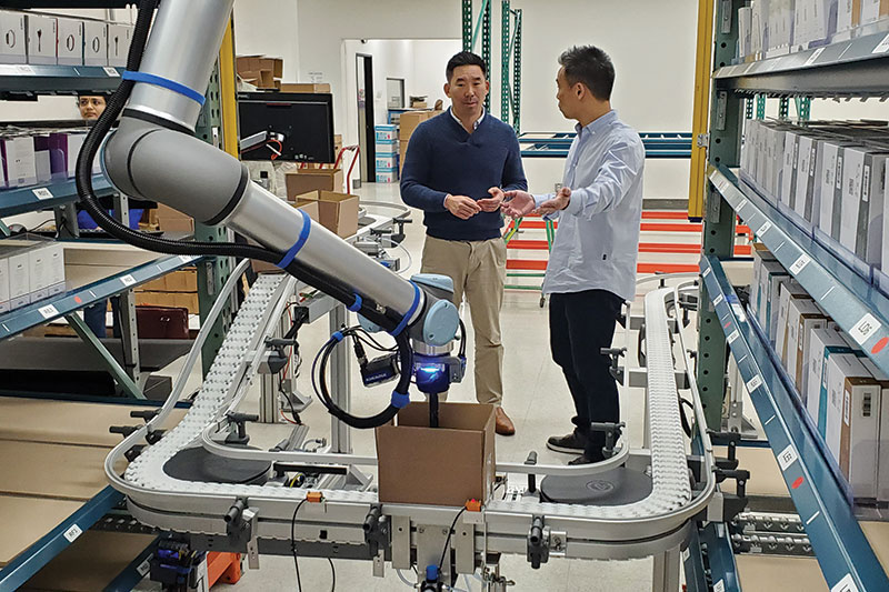 Brian Tu, CRO at DCL Logistics (at left), with Dave Tu, DCL’s president, along with one of the cobot-based pack out systems the company has deployed.